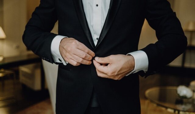 Person fastening the front button of a classic black tuxedo jacket