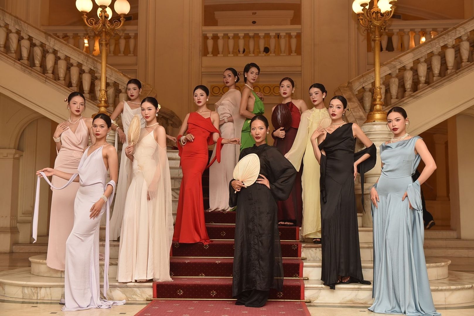 Models in elegant evening gowns pose on a grand marble staircase