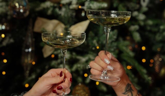 Two coupe glasses of sparkling drinks raised before a lit Christmas tree