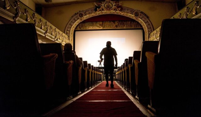 Silhouetted person walking toward a cinema screen during a screening